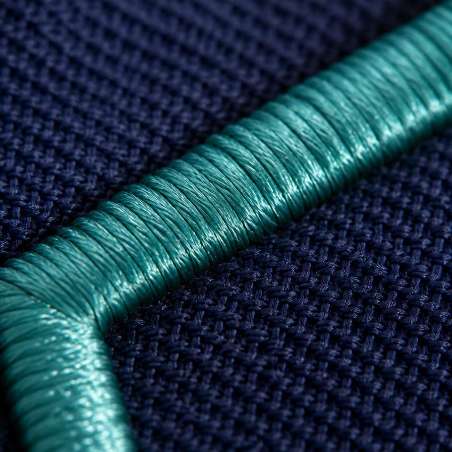 Macro close-up of teal satin-stitch embroidery on navy piqué polo fabric